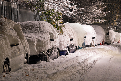 A number of parked cars covered in snow.
